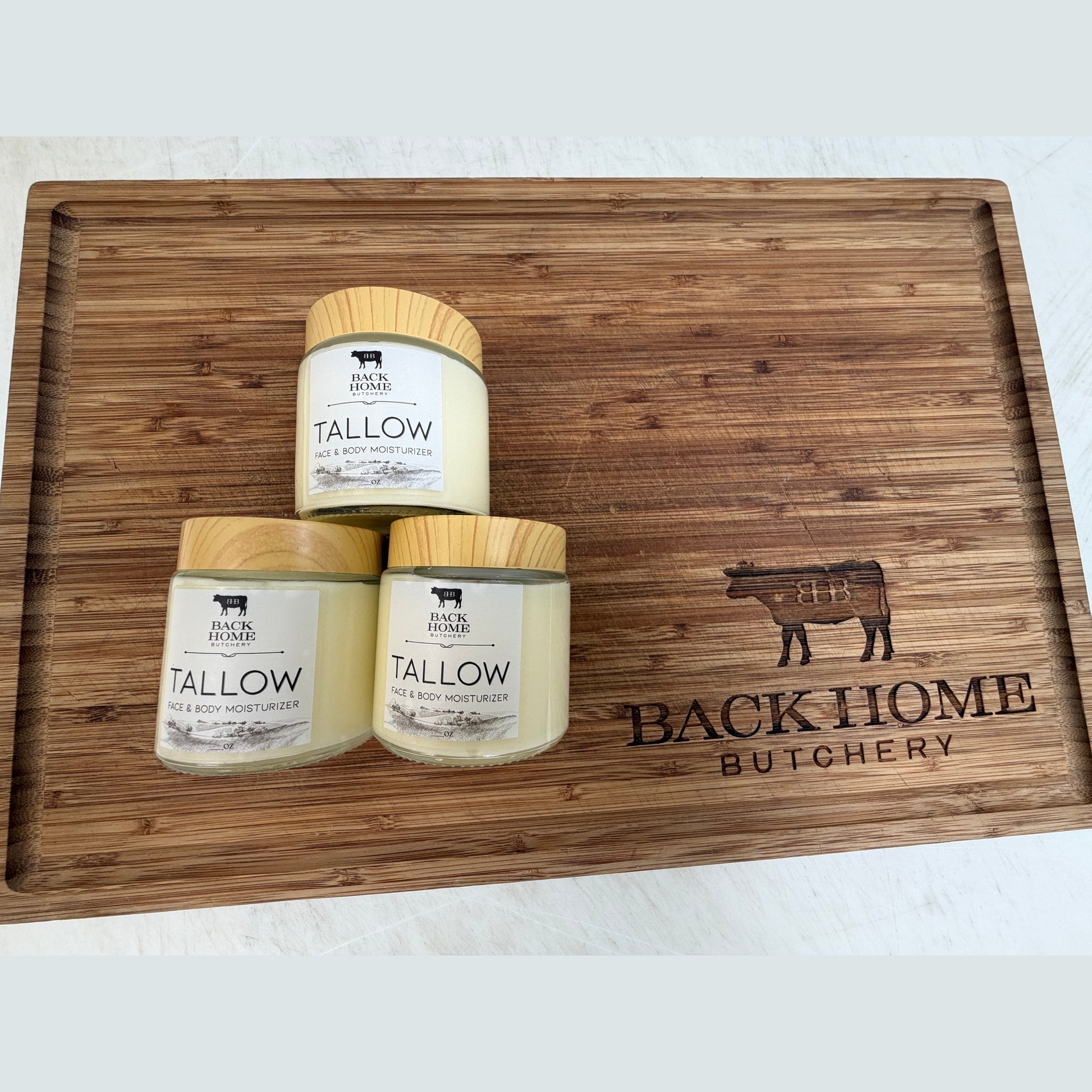 Three Grass Fed Beef Tallow Lotions on a wooden cutting board branded 'Back Home Butchery'.
